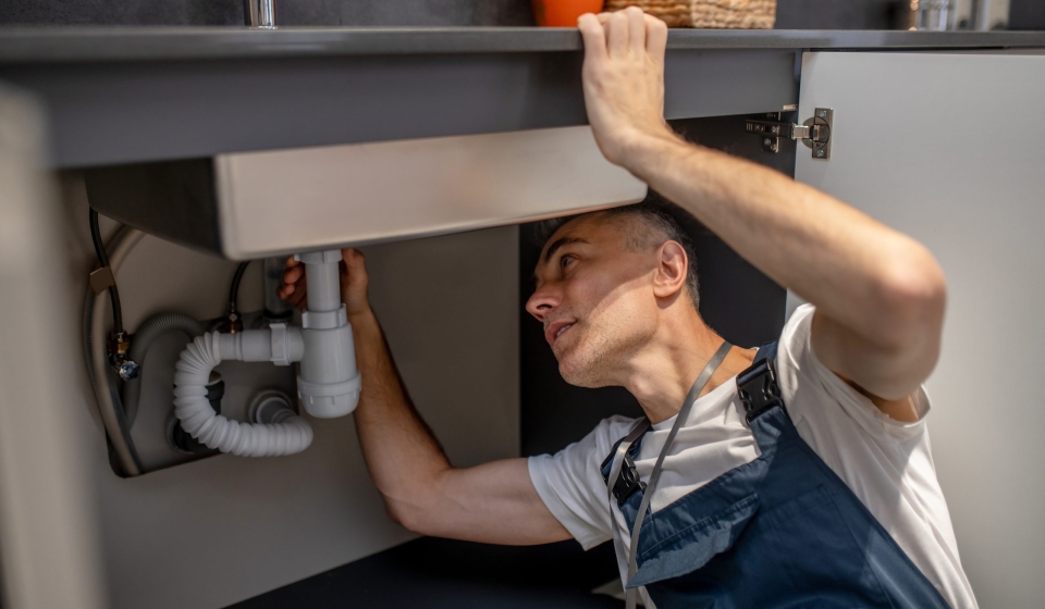 Plumber, repair. Experienced attentive middle-aged man carefully examining bottom of kitchen sink touching pipe with his hand diagnosing problem